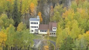 Une maison à deux étages entourée d’arbres aux feuilles d’automne.