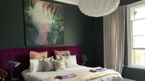 A bedroom with a large bed, a purple headboard, a painting above the bed, and a window with curtains. - Historical terrace house in the middle of Fitzroy (Fitzroy)