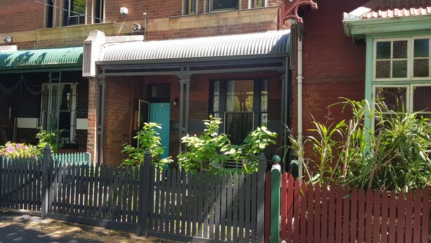 A brick building with a green awning, a white picket fence, and potted plants. - Historical terrace house in the middle of Fitzroy (Fitzroy)