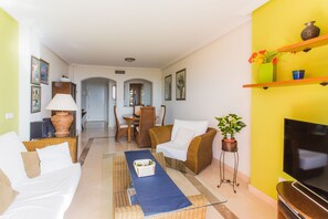 Una sala de estar con un sofá, sillones, una mesa de centro, un televisor y un comedor con sillas y una mesa.