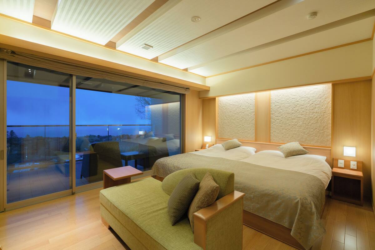 A hotel room with a large bed, a sofa, a desk, and a sliding glass door leading to an outdoor area.