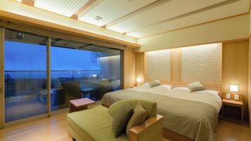 A hotel room with a large bed, a sofa, a desk, and a sliding glass door leading to an outdoor area.