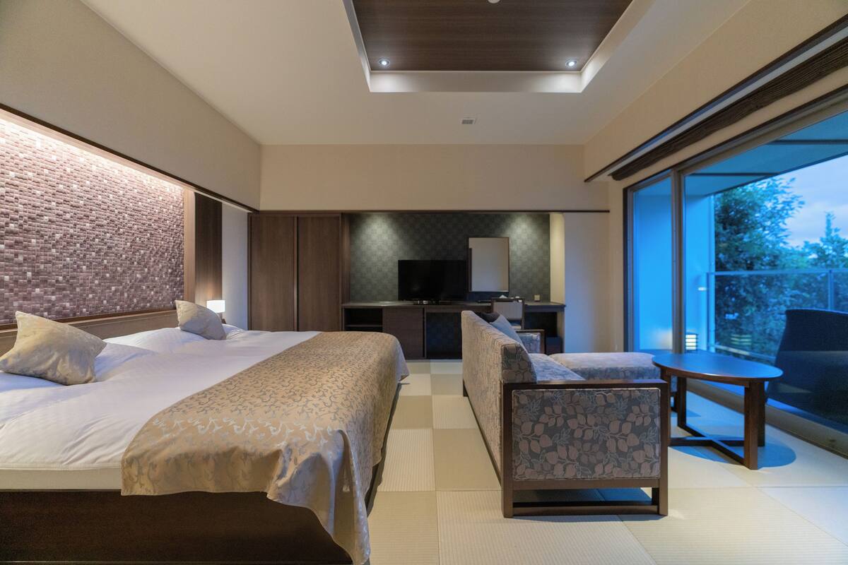 A modern hotel room with two beds, a desk, a chair, and a large window offering a view.