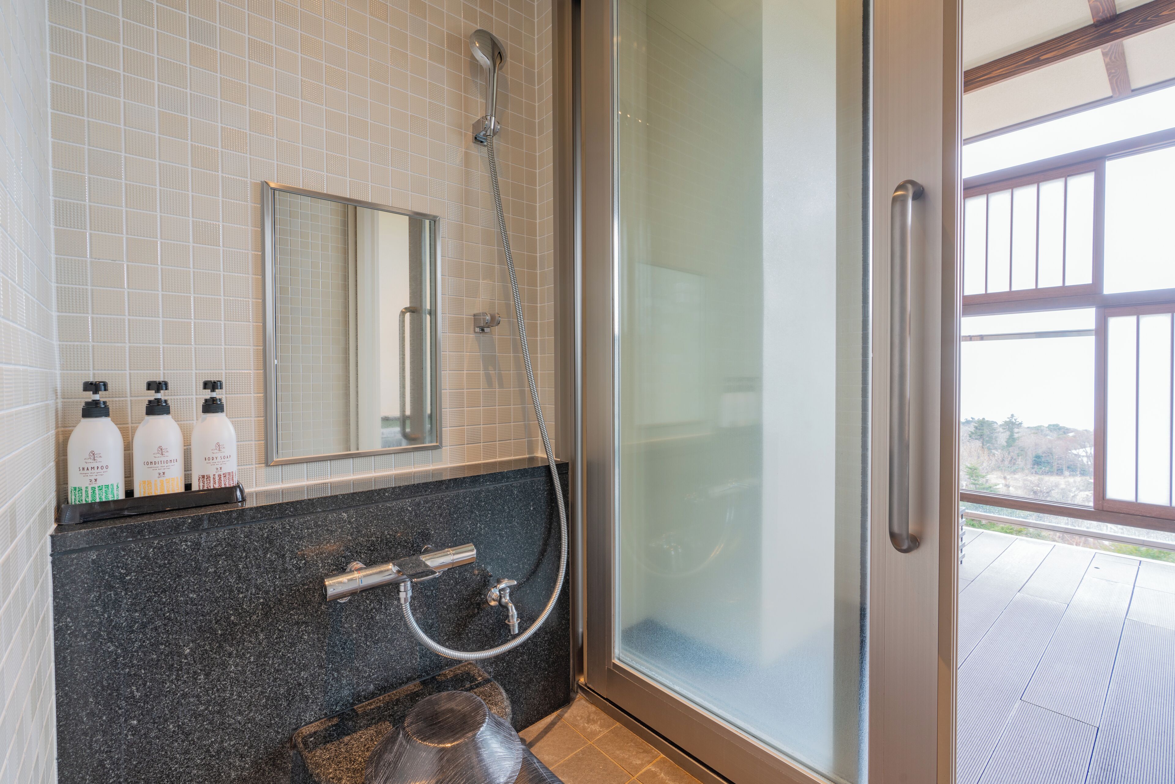 A bathroom with a glass shower enclosure, a sink with a faucet, and three bottles of shampoo on the counter.