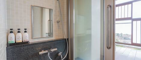 A bathroom with a glass shower enclosure, a sink with a faucet, and three bottles of shampoo on the counter.