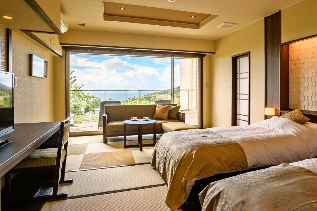 A hotel room with a balcony, a desk, two beds, and a view of the outdoors.