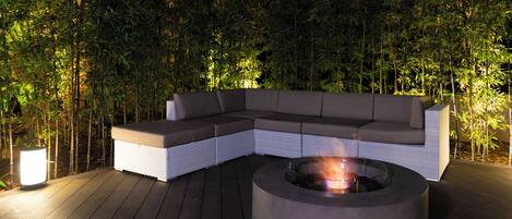 A modern outdoor seating area with a built-in fire pit and a white cushioned sofa.