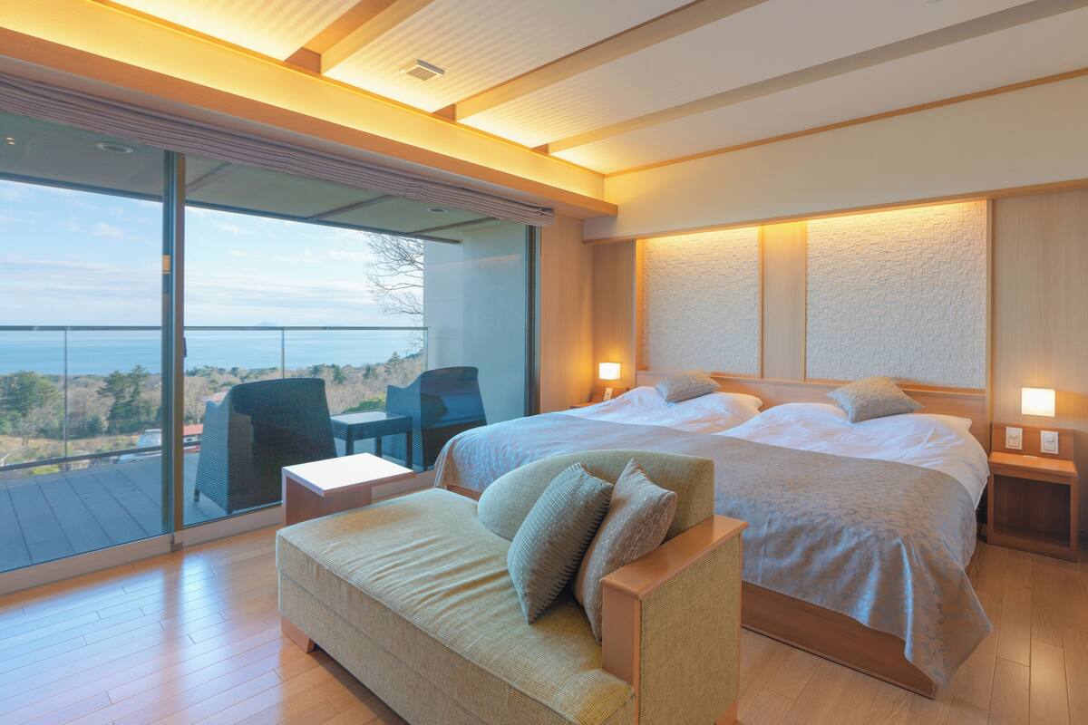 A modern bedroom with a large bed, a sofa, a desk, and a view of the outdoors.