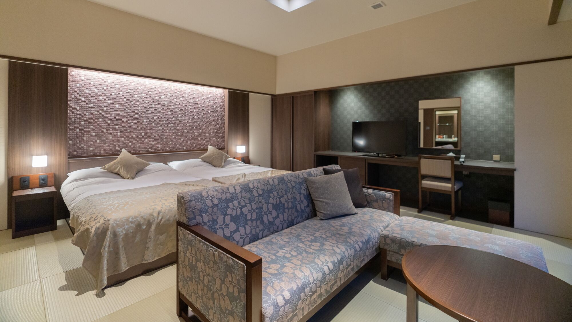 A modern hotel room with a large bed, a sofa, a TV, and a desk.