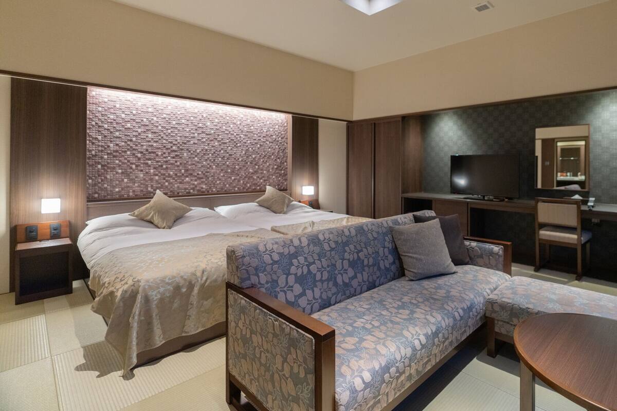 A modern hotel room with a large bed, a sofa, a TV, and a desk.