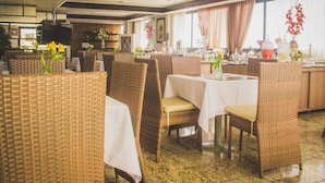 A restaurant with wicker chairs and tables, a television, and decorative flowers. - JOH Blue Ocean Hotel (Fortaleza)