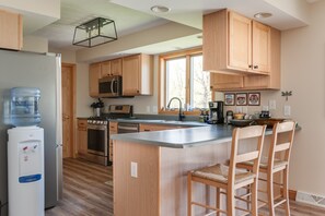 Une cuisine moderne avec des meubles en bois, un réfrigérateur en acier inoxydable, un distributeur d’eau, un four à micro-ondes, une cuisinière et un grand îlot central doté de tabourets de bar.