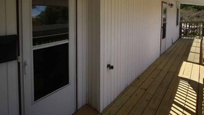 Un edificio blanco con terraza de madera, puerta corredera de vidrio y una ventana pequeña.