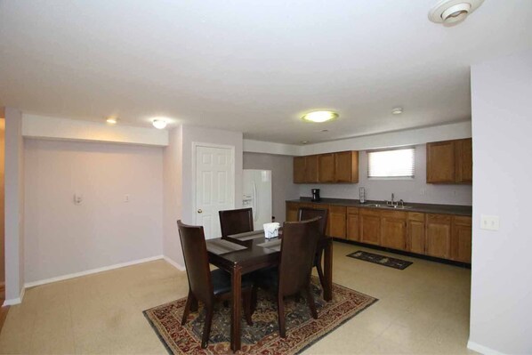A dining area with a table and chairs, a kitchen with wooden cabinets, and a white door.