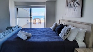 Ett sovrum med en stor säng, utsikt över stranden och en tavla på väggen.