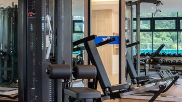 Un gimnasio con diferentes máquinas de ejercicio, un espejo grande y vistas al exterior con vegetación.