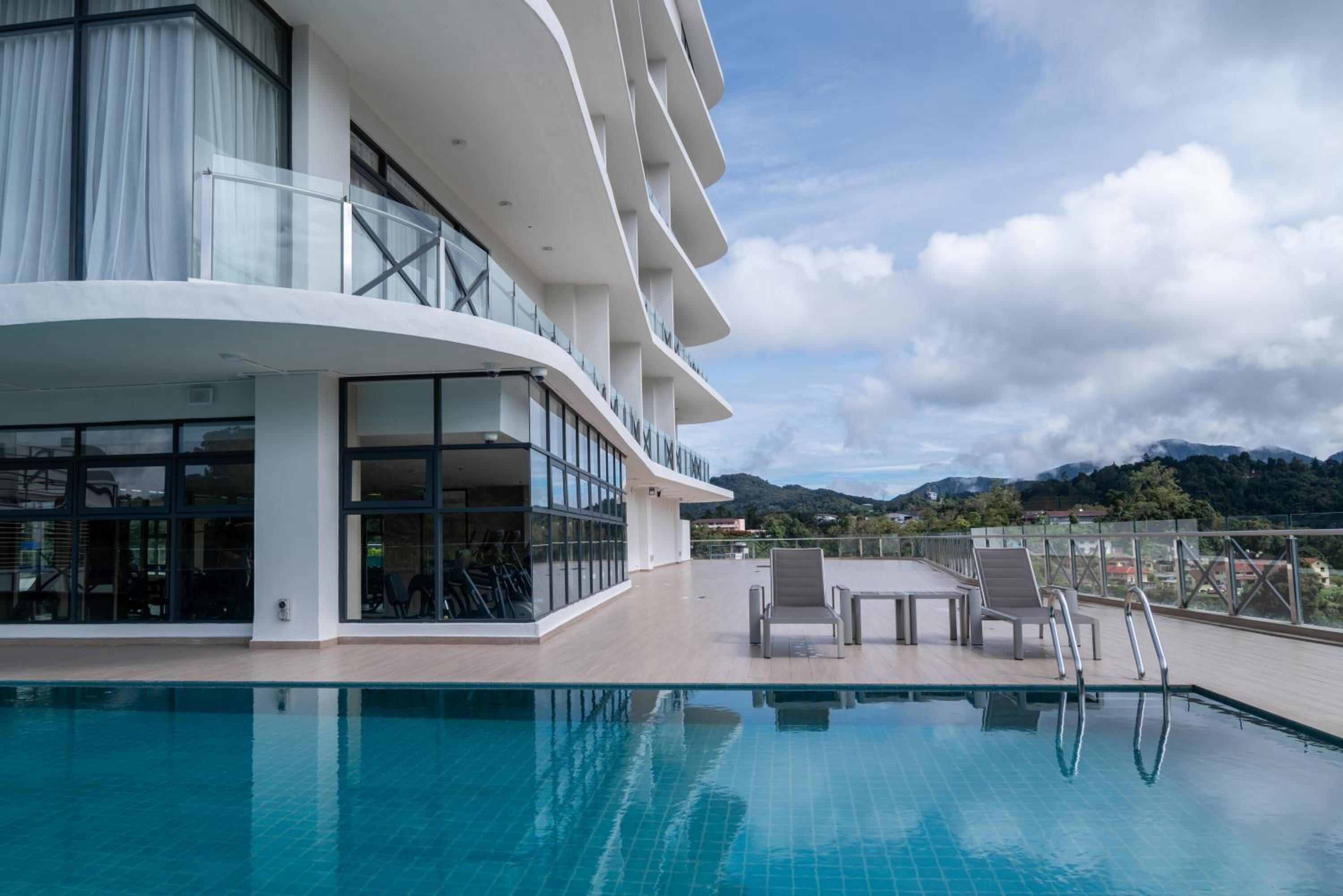 Un hotel moderno con zona de piscina, mobiliario exterior y vistas a montañas.