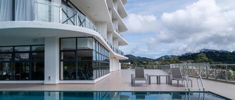 Un hotel moderno con zona de piscina, mobiliario exterior y vistas a montañas.