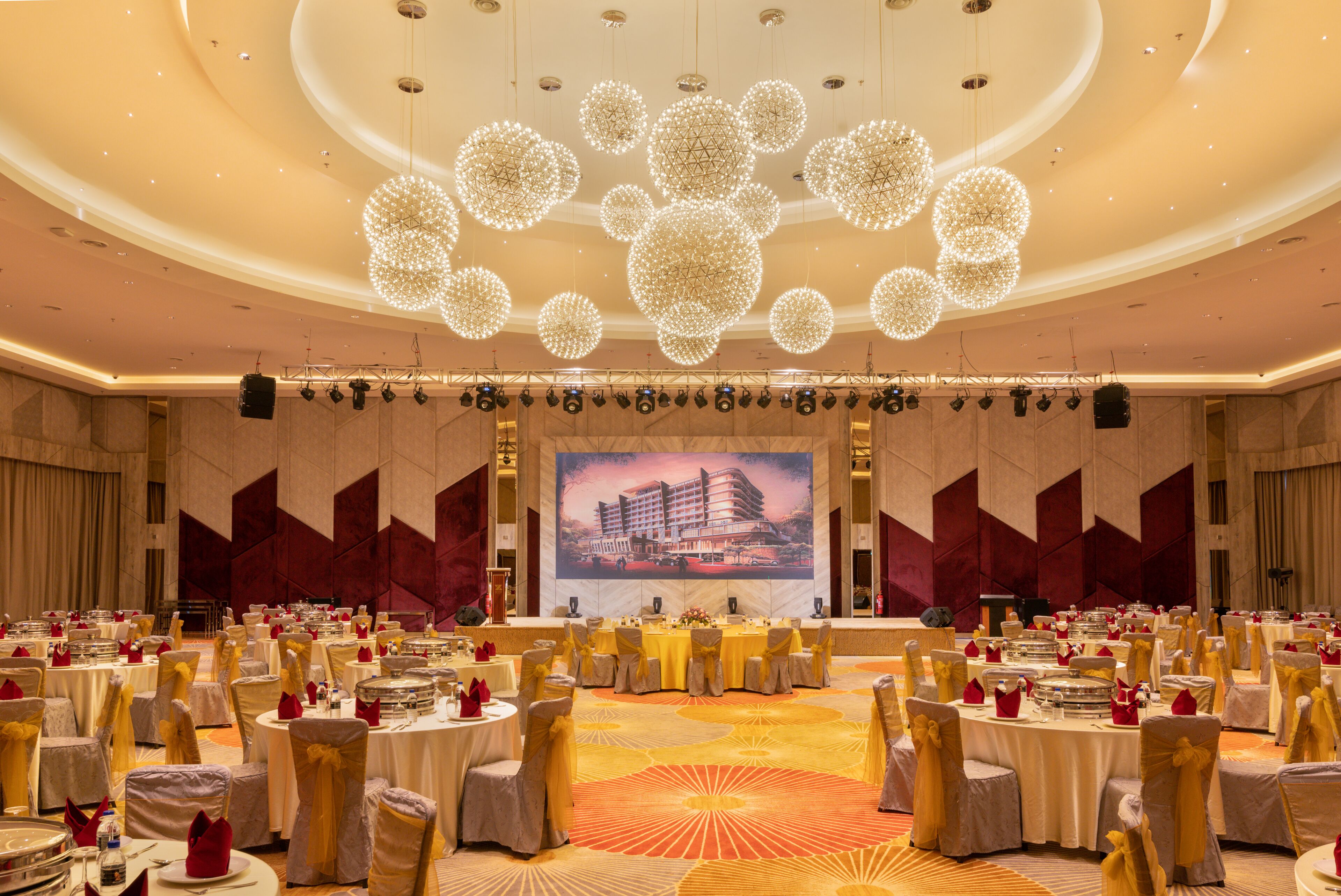 Un gran salón de banquetes con mesas redondas, sillas y un escenario con una pantalla grande.