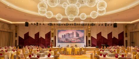Un gran salón de banquetes con mesas redondas, sillas y un escenario con una pantalla grande.