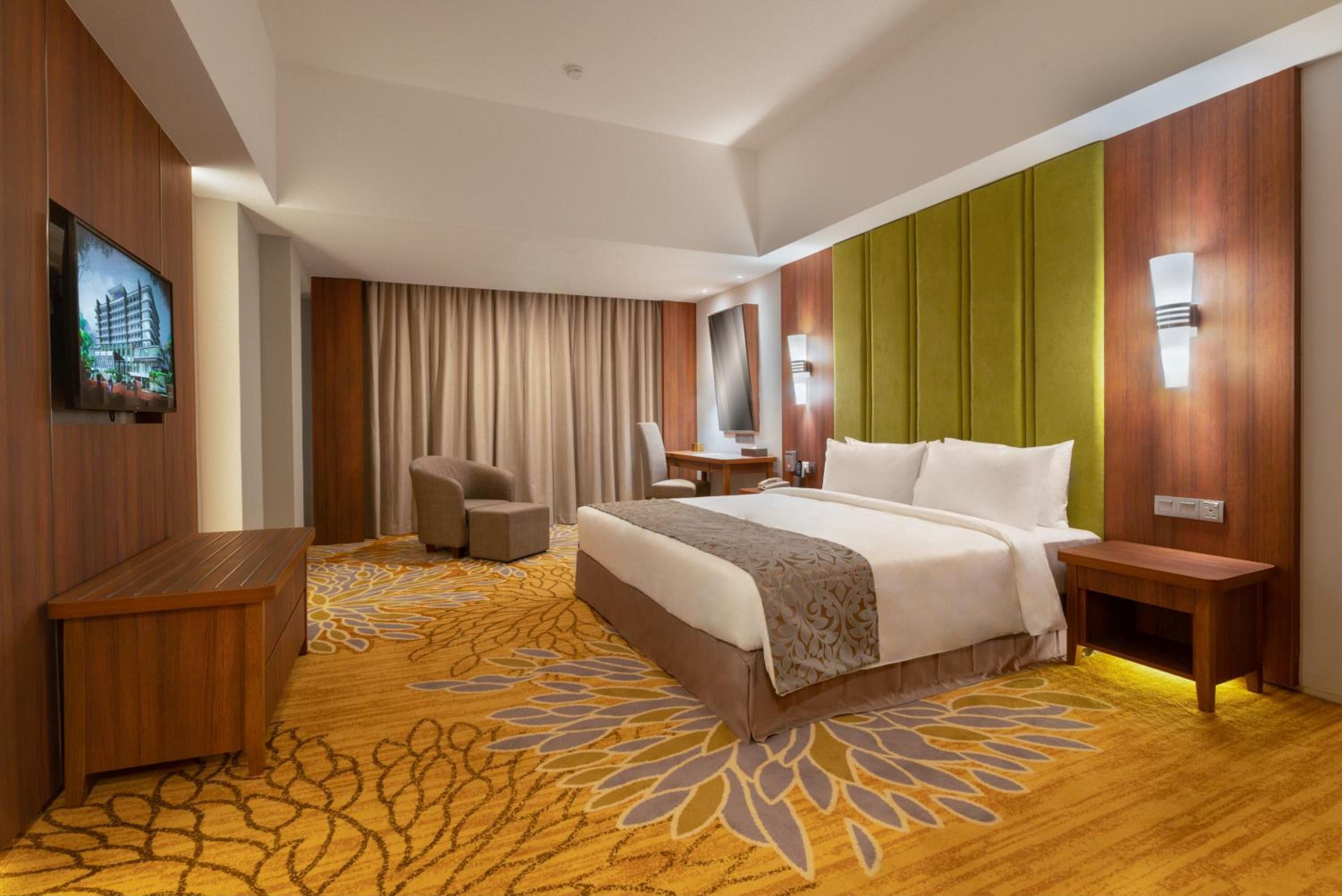 A hotel room with a large bed, a desk, a chair, a television, and a view of a building outside.
