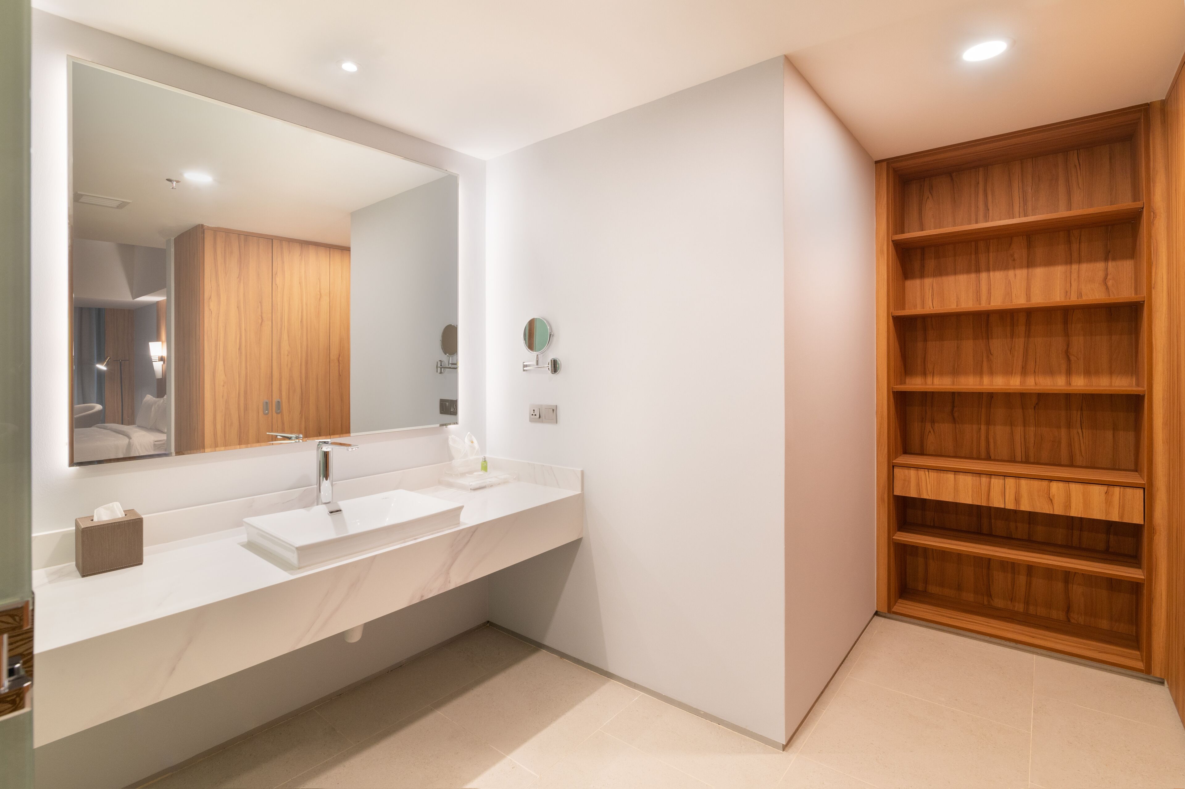 A modern bathroom with a white vanity, a large mirror, and wooden shelving.