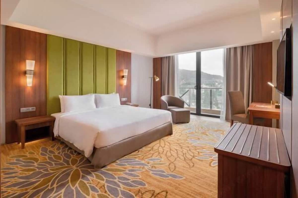 A hotel room with a large bed, a desk, a chair, and a view of the outdoors.