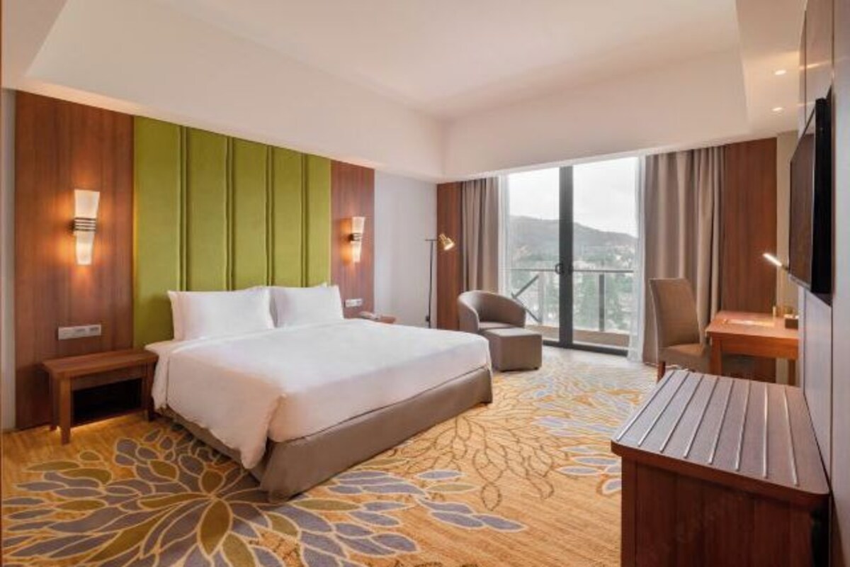 A hotel room with a large bed, a desk, a chair, and a view of the outdoors.