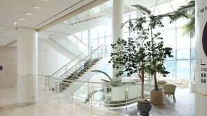 Un lobby espacioso con una escalera central, ventanas amplias y plantas de interior.