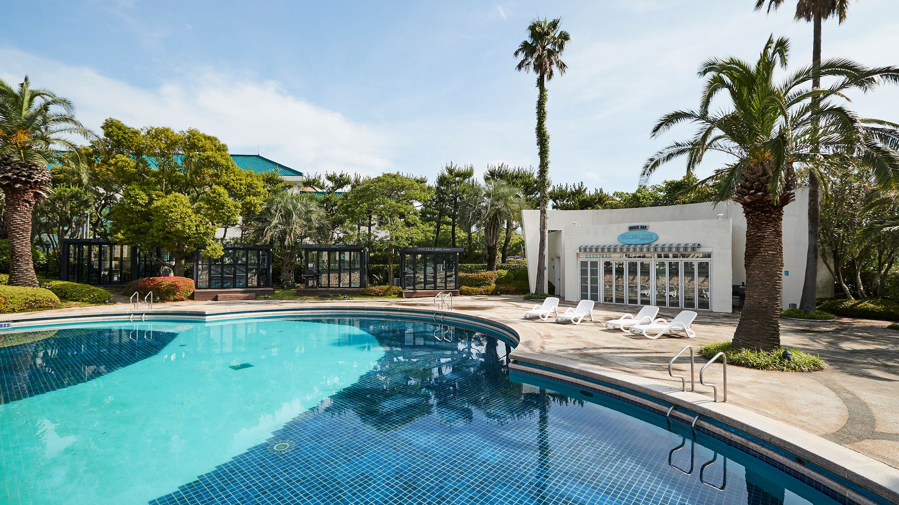 A swimming pool with lounge chairs, a self-service BBQ zone, and a building with a sign.