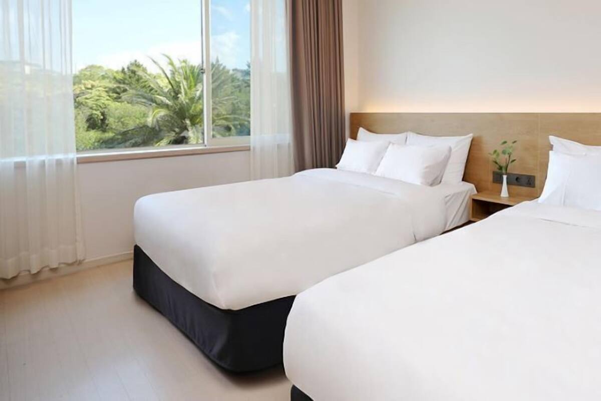 Habitación de hotel con dos camas, una mesita de noche y una ventana con cortinas.