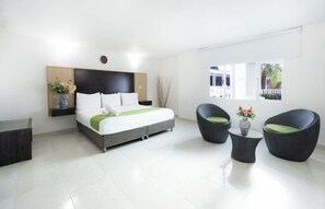 Una habitación de hotel moderna con una cama, dos mesitas auxiliares, una silla y un ventanal.