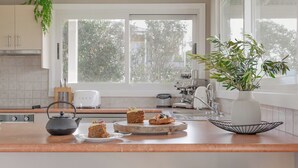 Eine moderne Küche mit einer großen Kochinsel, zwei Barhocker, einer Kaffeemaschine und einem Blumentopf.