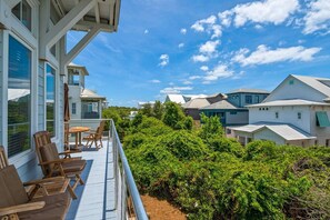 A wooden deck with outdoor furniture, surrounded by lush greenery and a view of neighboring houses.
