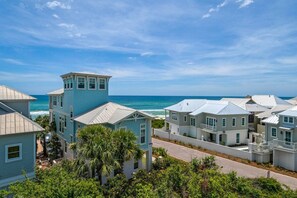 A coastal residential area with houses featuring light blue and white exteriors, a prominent tower-like structure, and a view of the ocean.