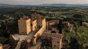 Un château de pierre historique, doté de murs fortifiés, entouré de collines verdoyantes et bordé d’une route sinueuse.