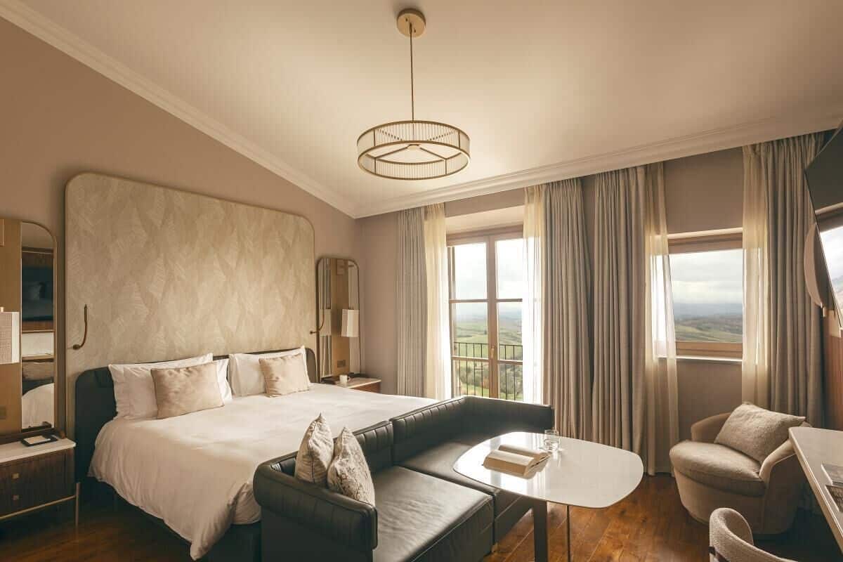 Ett hotellrum med en stor säng, en soffa, ett litet bord och utsikt över landsbygden.