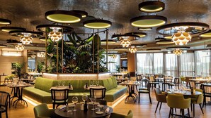 Un restaurant avec des tables rondes, des sièges verts et des luminaires circulaires suspendus au plafond.