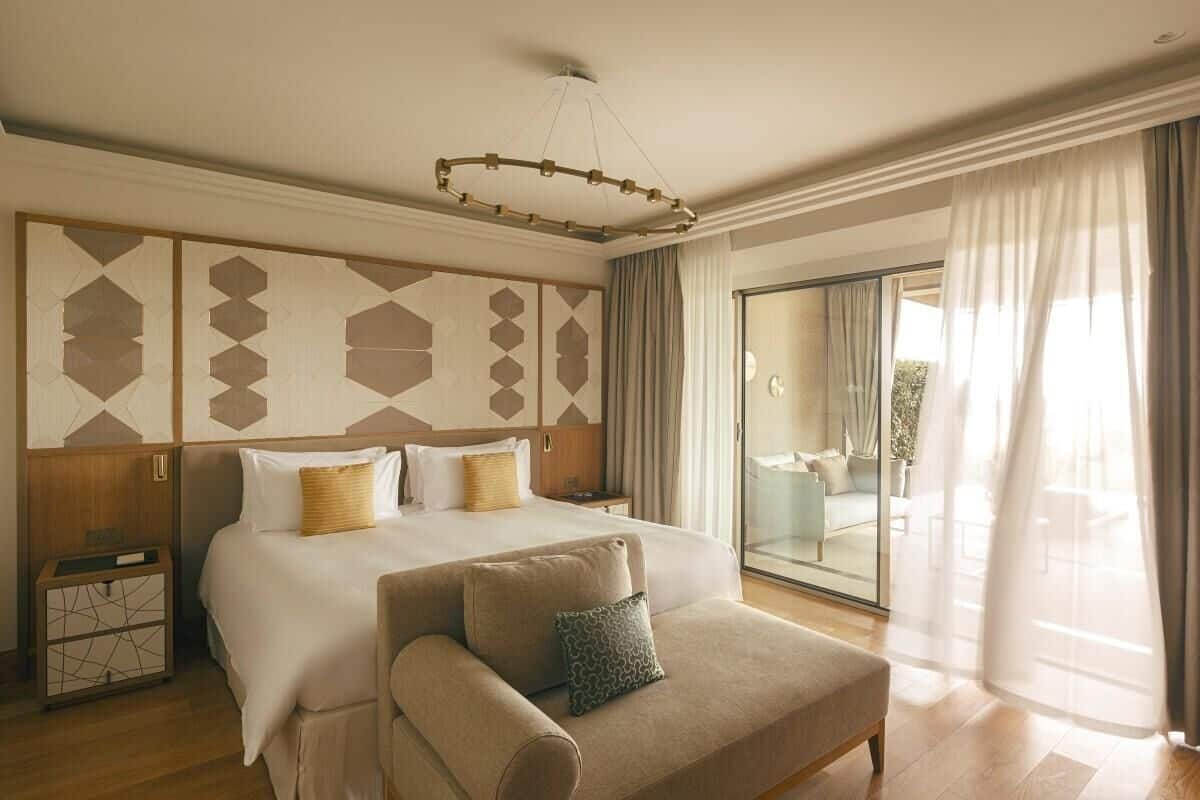 Ett hotellrum med en stor säng, en soffa, en glasdörr som leder ut till en balkong och en vägg med ett geometriskt mönster.