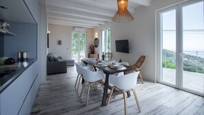 A modern dining area with a wooden table and white chairs, a large window with a view, and a ceiling with exposed beams.