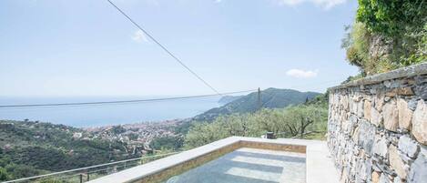 A swimming pool with a stone wall and a view of a coastal town.