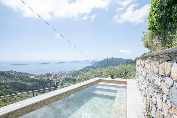 A swimming pool with a stone wall and a view of a coastal town.