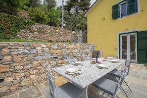 A stone wall with a stone bench and a table set for two with plates, glasses, and cutlery.
