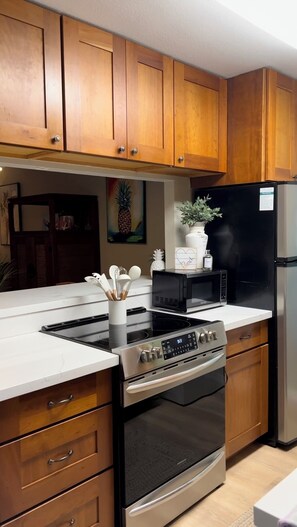 Une cuisine moderne avec des meubles en bois, un réfrigérateur noir, un four à micro-ondes et une cuisinière en acier inoxydable.
