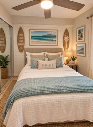 A bedroom with a bed, a ceiling fan, a nightstand with a lamp, and wall decorations including surfboards and a framed picture of a beach. - Maui Ocean + Jeep (Kihei)