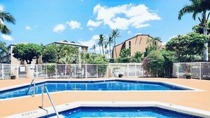 A swimming pool with a white fence, surrounded by palm trees and buildings. - 2 Bedroom Ocean Jeep  (Kihei)
