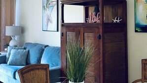 A living room with a glass-top table, wicker chairs, a blue sofa, a wooden cabinet with 'Aloha' written on it, and a ceiling fan. - 2 Bedroom Ocean Jeep  (Kihei)