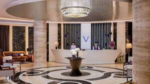 Una hall moderna con una reception, un tavolo decorativo centrale e un lampadario.