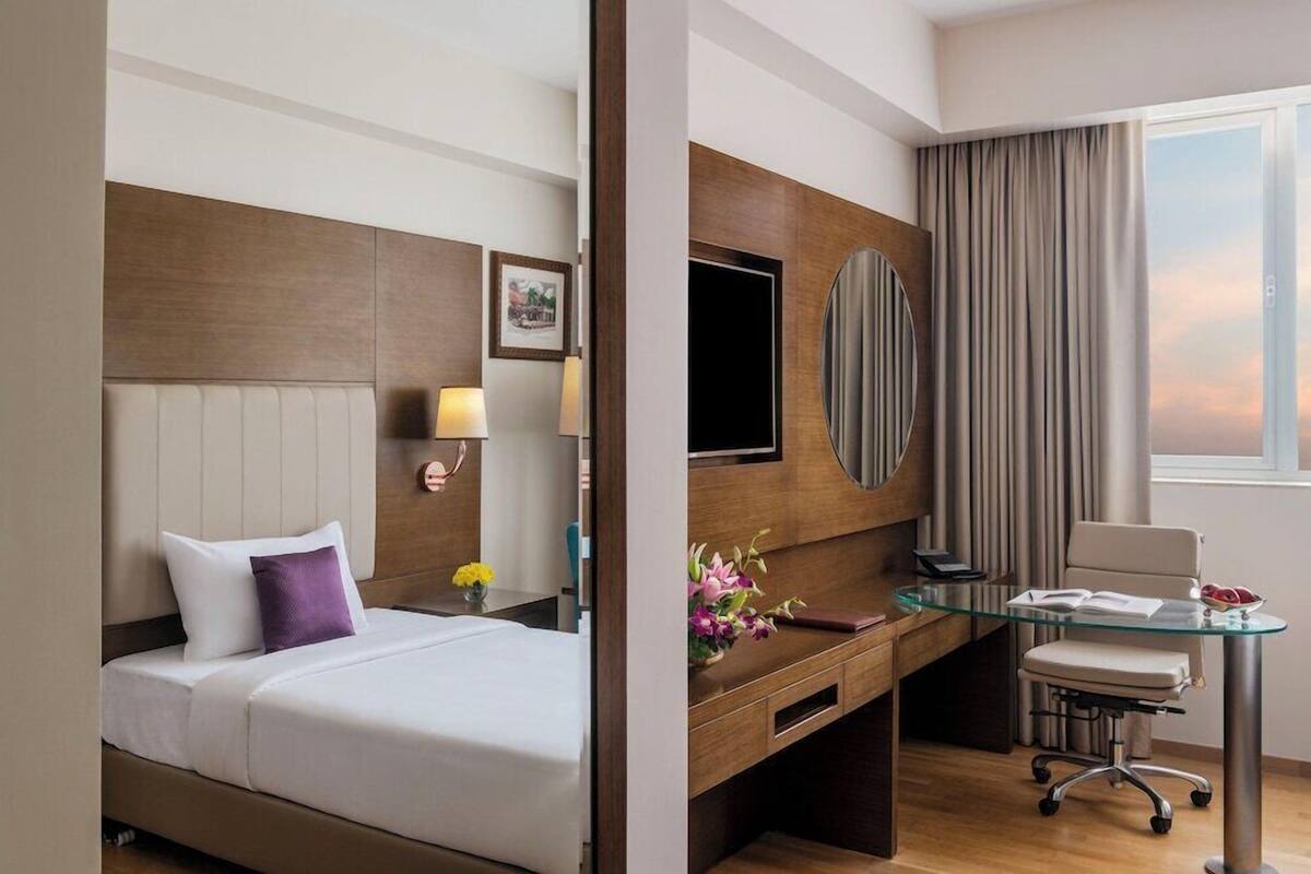 Habitación de hotel con cama, escritorio, silla, televisor y ventana con cortinas.