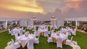 Una sala da banchetto all'aperto con tavoli rotondi e sedie bianche, con il tramonto sullo sfondo.